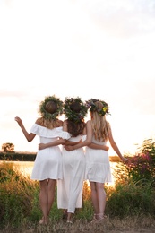 Young women wearing wreaths made of flowers outdoors at sunset, back view