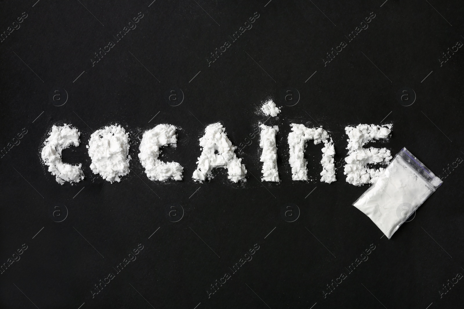 Photo of Word Cocaine written with white powder and full plastic bag on black background, top view