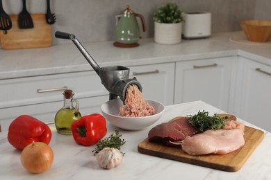 Metal meat grinder with chicken mince and products on white marble table in kitchen