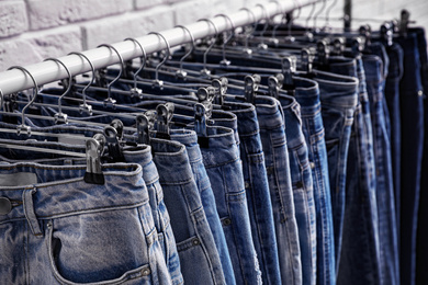 Rack with stylish jeans near brick wall, closeup