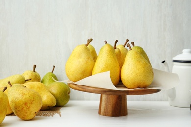 Stand with fresh ripe pears on table against light background