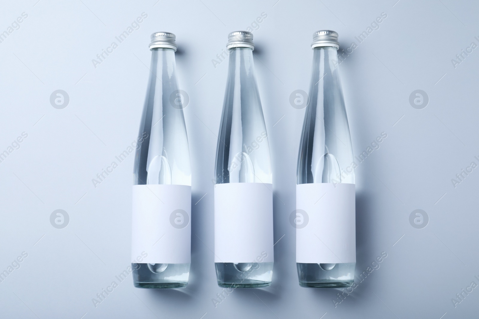 Photo of Glass bottles with soda water on light background, flat lay