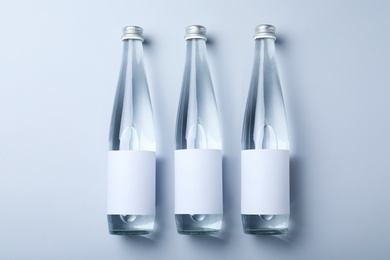 Glass bottles with soda water on light background, flat lay