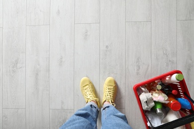 Photo of Woman and shopping basket with groceries on white wooden floor, top view. Space for text
