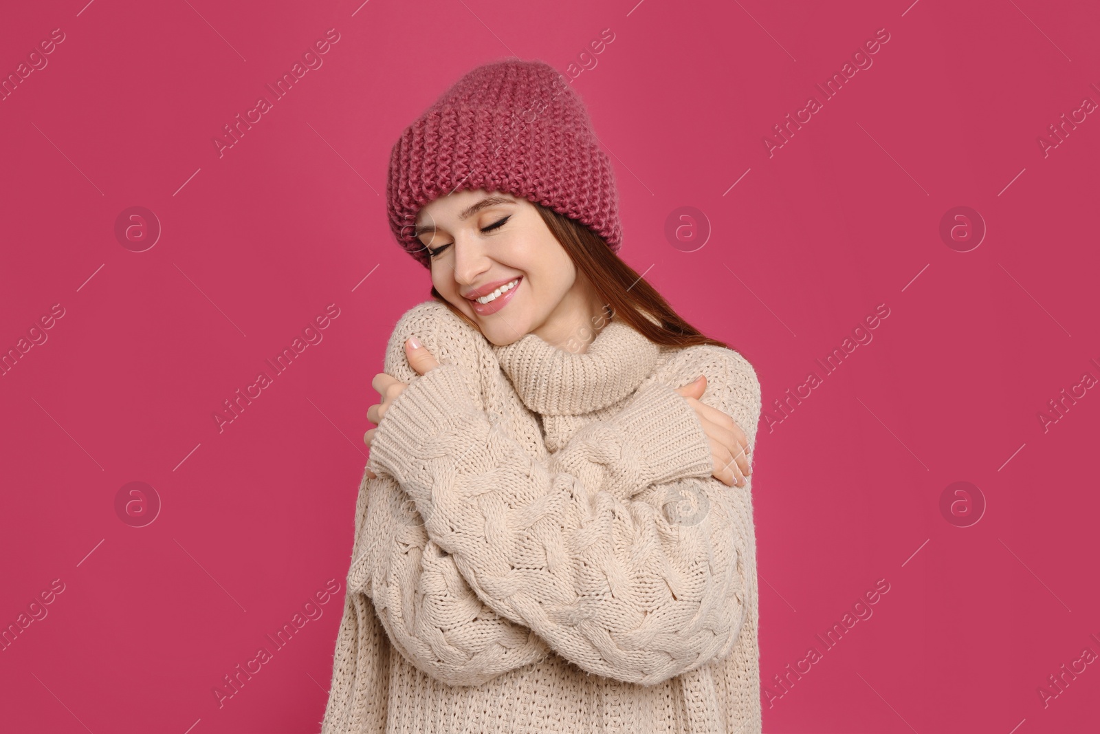 Photo of Young woman wearing warm sweater and hat on crimson background. Winter season