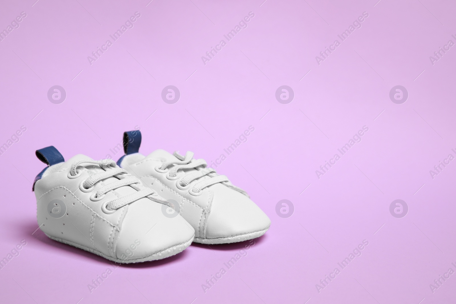 Photo of Cute baby shoes on violet background, space for text