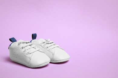 Photo of Cute baby shoes on violet background, space for text