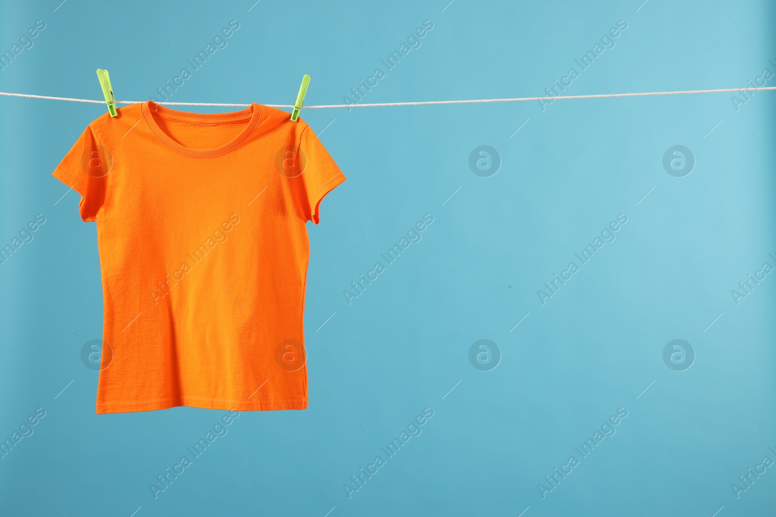 Photo of One orange t-shirt drying on washing line against light blue background. Space for text