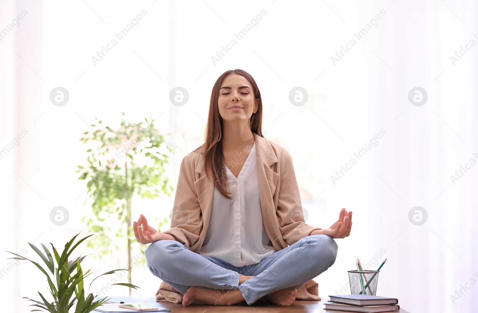 Photo of Young businesswoman meditating at workplace. Zen concept