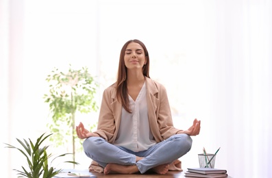 Young businesswoman meditating at workplace. Zen concept