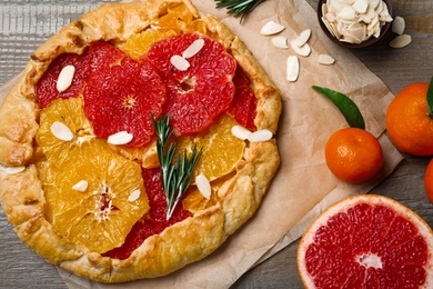 Photo of Delicious galette with citrus fruits, almond flakes and rosemary on wooden table, flat lay
