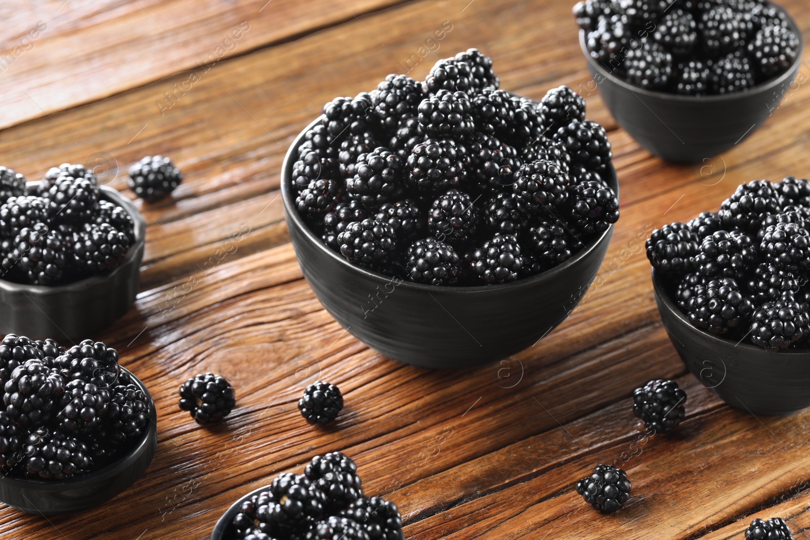 Photo of Ripe blackberries in bowls on wooden table