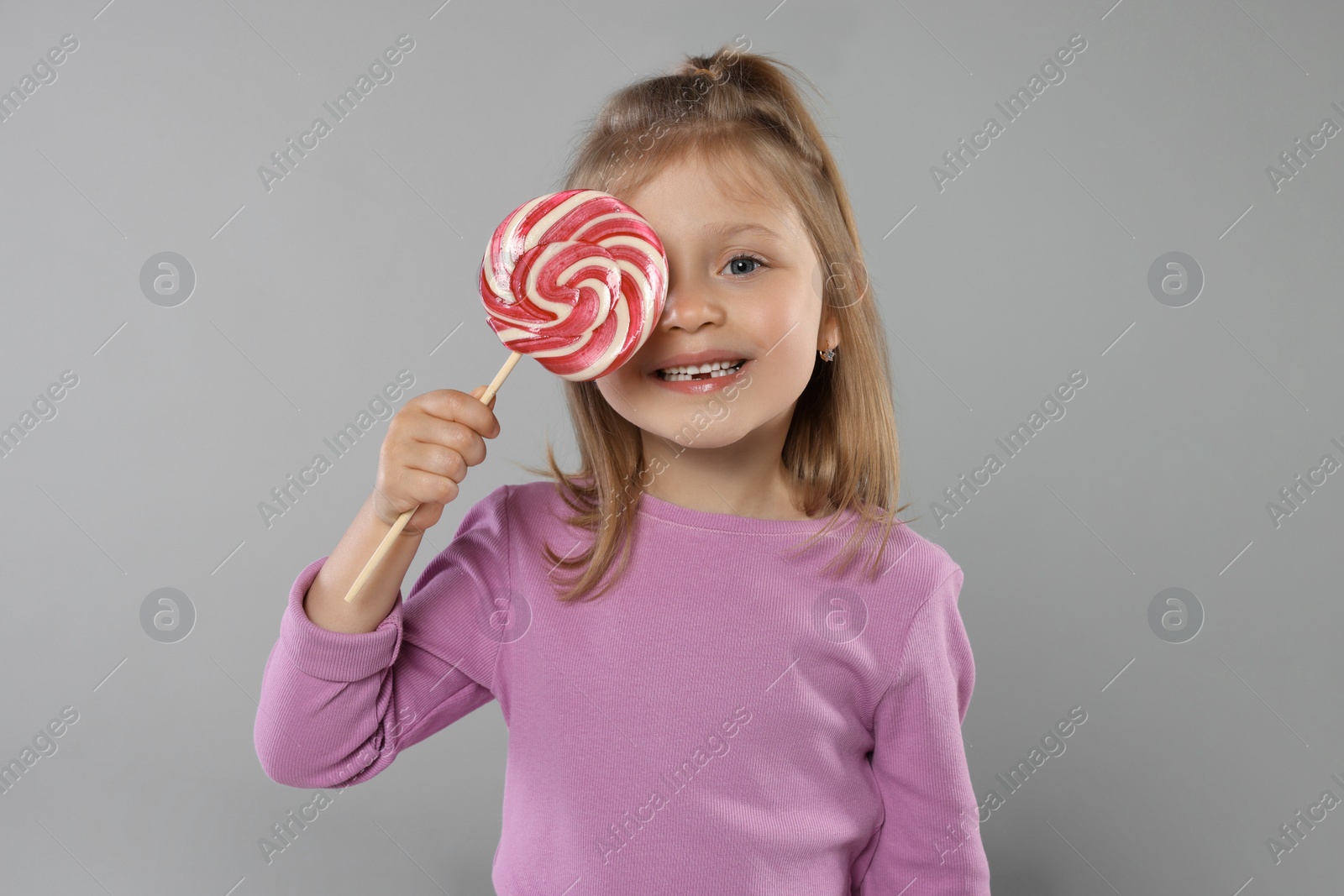 Photo of Happy girl covering eye with lollipop on light grey background