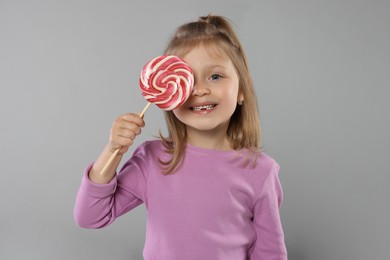 Happy girl covering eye with lollipop on light grey background