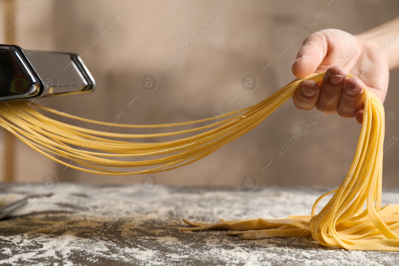 Photo of Woman preparing noodles with pasta maker machine at table, closeup