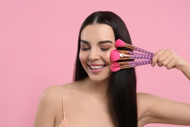 Photo of Happy woman with different makeup brushes on pink background