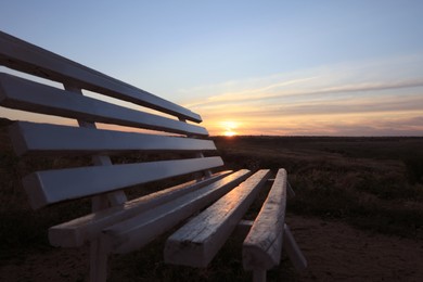 Photo of Wooden bench in field at sunrise, closeup. Early morning landscape