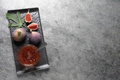 Photo of Glass bowl with tasty sweet jam and fresh figs on grey table, top view. Space for text