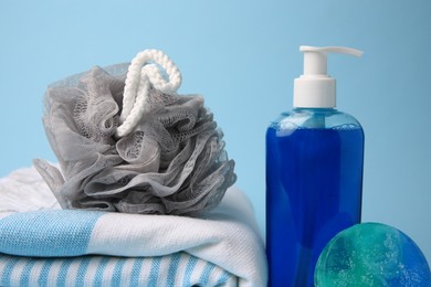 Photo of Grey shower puff, cosmetic products and towel on light blue background, closeup