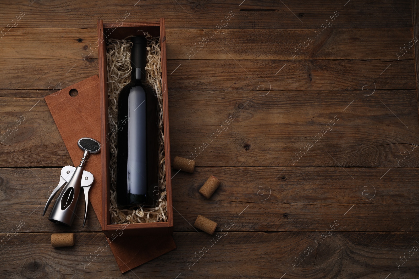 Photo of Box with wine bottle, wing corkscrew and corks on wooden table, flat lay. Space for text