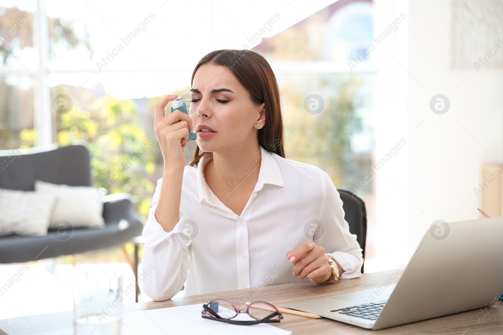 Photo of Young woman with asthma inhaler at table in light room