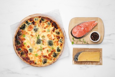 Delicious homemade quiche and ingredients on white marble table, flat lay