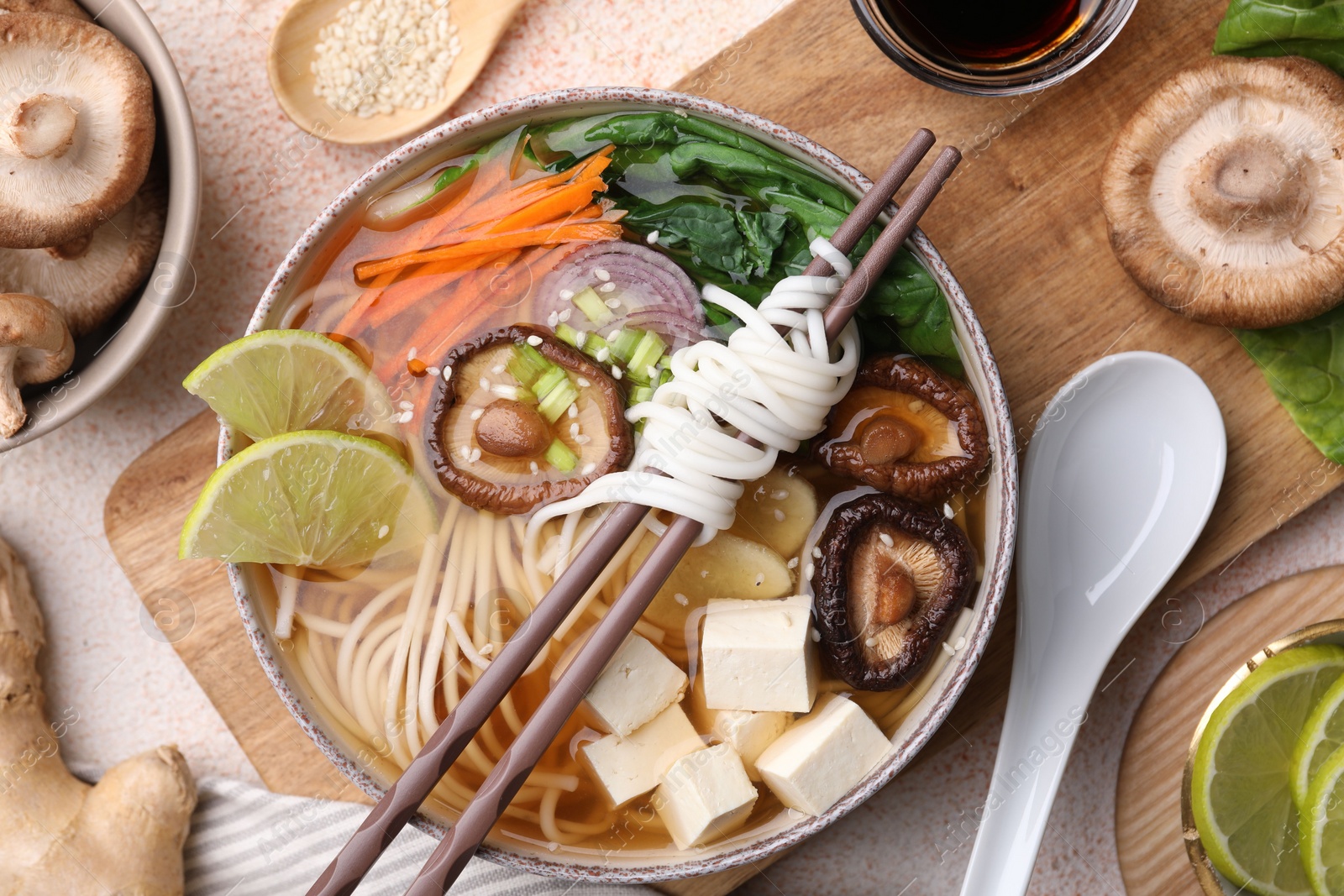 Photo of Vegetarian ramen, chopsticks and ingredients on light textured table, flat lay