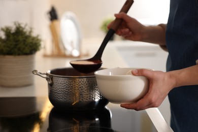 Woman pouring tasty soup into bowl at countertop in kitchen, closeup