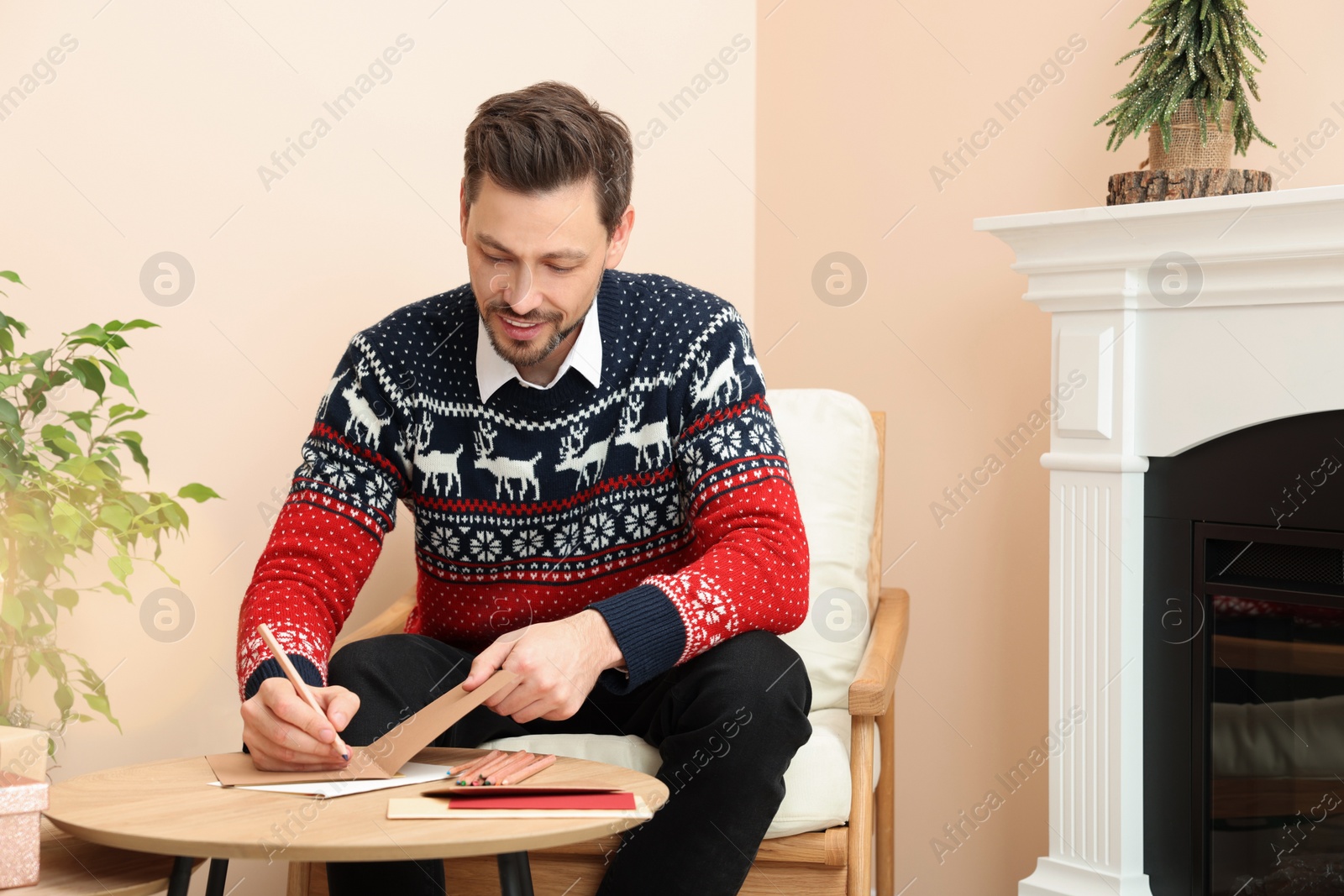 Photo of Happy man writing wishes in Christmas greeting card in living room