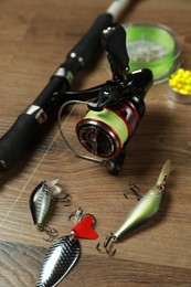 Photo of Fishing rod with spinning reel and baits on wooden background, closeup