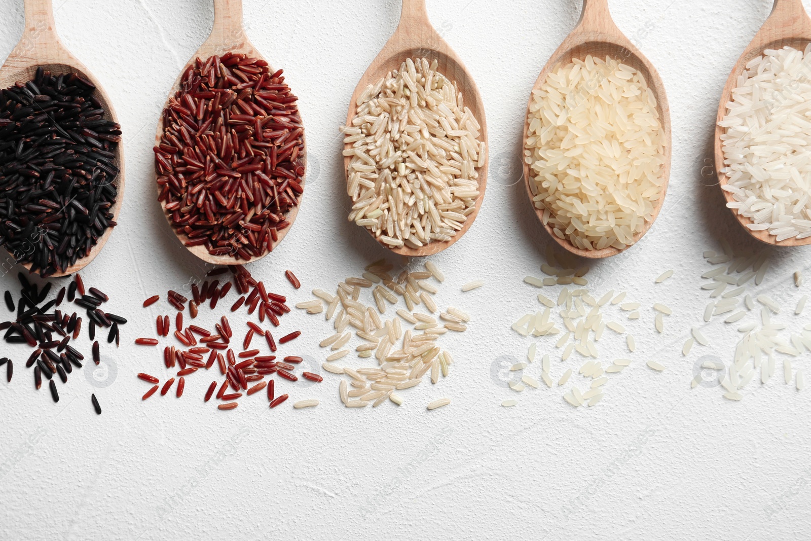 Photo of Flat lay composition with brown and other types of rice in spoons on white background