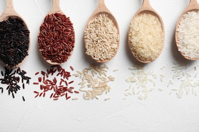 Flat lay composition with brown and other types of rice in spoons on white background