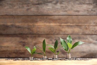 Stacked coins and young green plants on wooden table, space for text