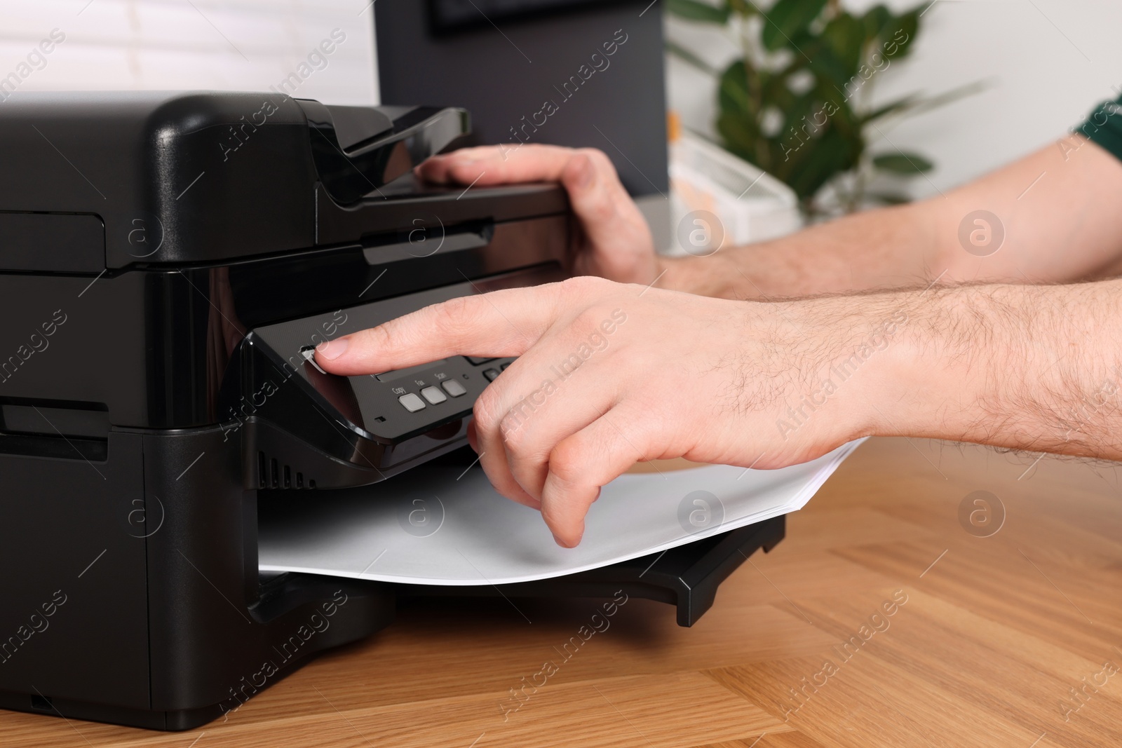 Photo of Man using modern printer at wooden table indoors, closeup