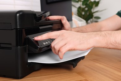 Photo of Man using modern printer at wooden table indoors, closeup