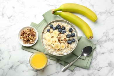 Tasty oatmeal with banana, blueberries, walnuts and milk served in bowl on white marble table, flat lay