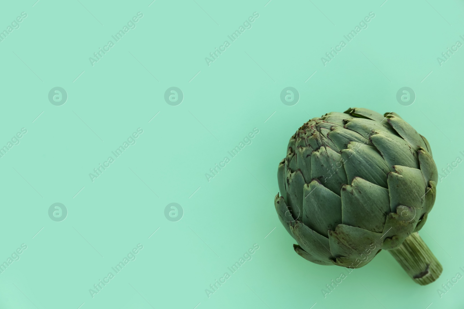 Photo of Whole fresh raw artichoke on green background, top view. Space for text