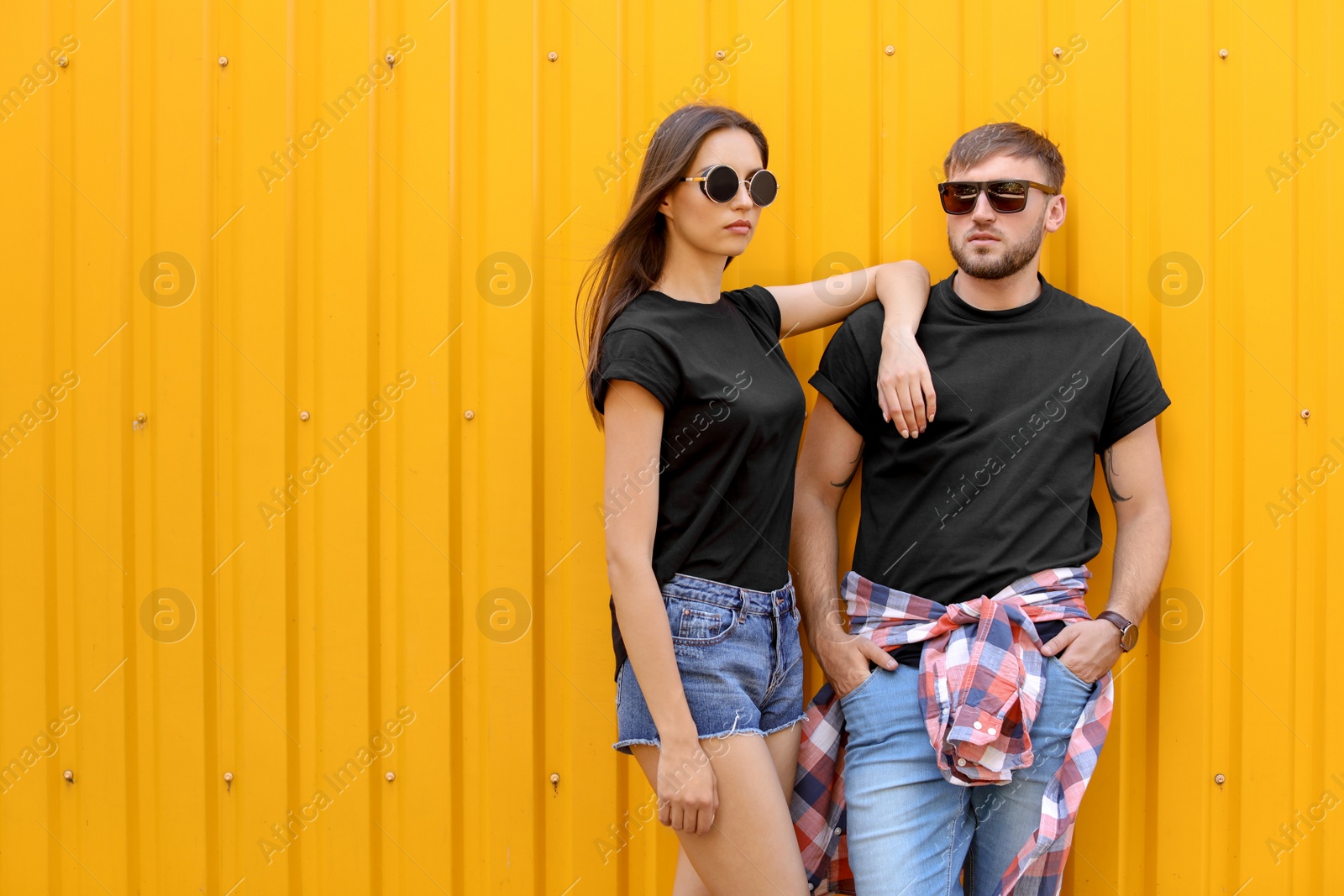 Photo of Young couple wearing black t-shirts near color wall on street