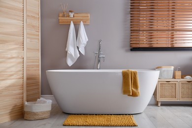 Photo of Soft orange mat on floor near tub in bathroom. Interior design