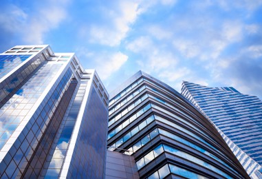 Image of Beautiful blue sky with clouds reflecting in windows. Low angle view of modern buildings