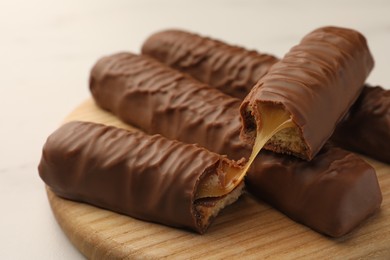 Photo of Sweet tasty chocolate bars with caramel on wooden board, closeup