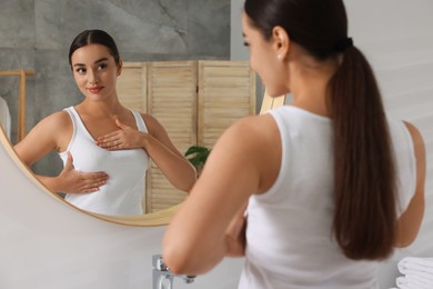 Beautiful young woman doing breast self-examination near mirror in bathroom