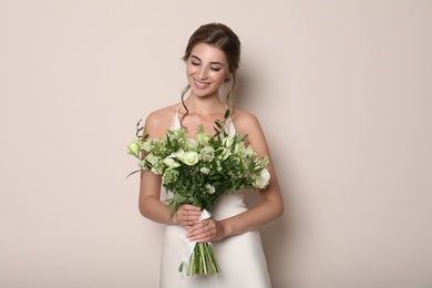 Young bride wearing wedding dress with beautiful bouquet on beige background