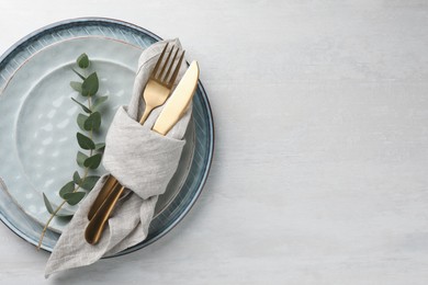 Stylish setting with cutlery, napkin, eucalyptus branch and plates on white table, top view. Space for text