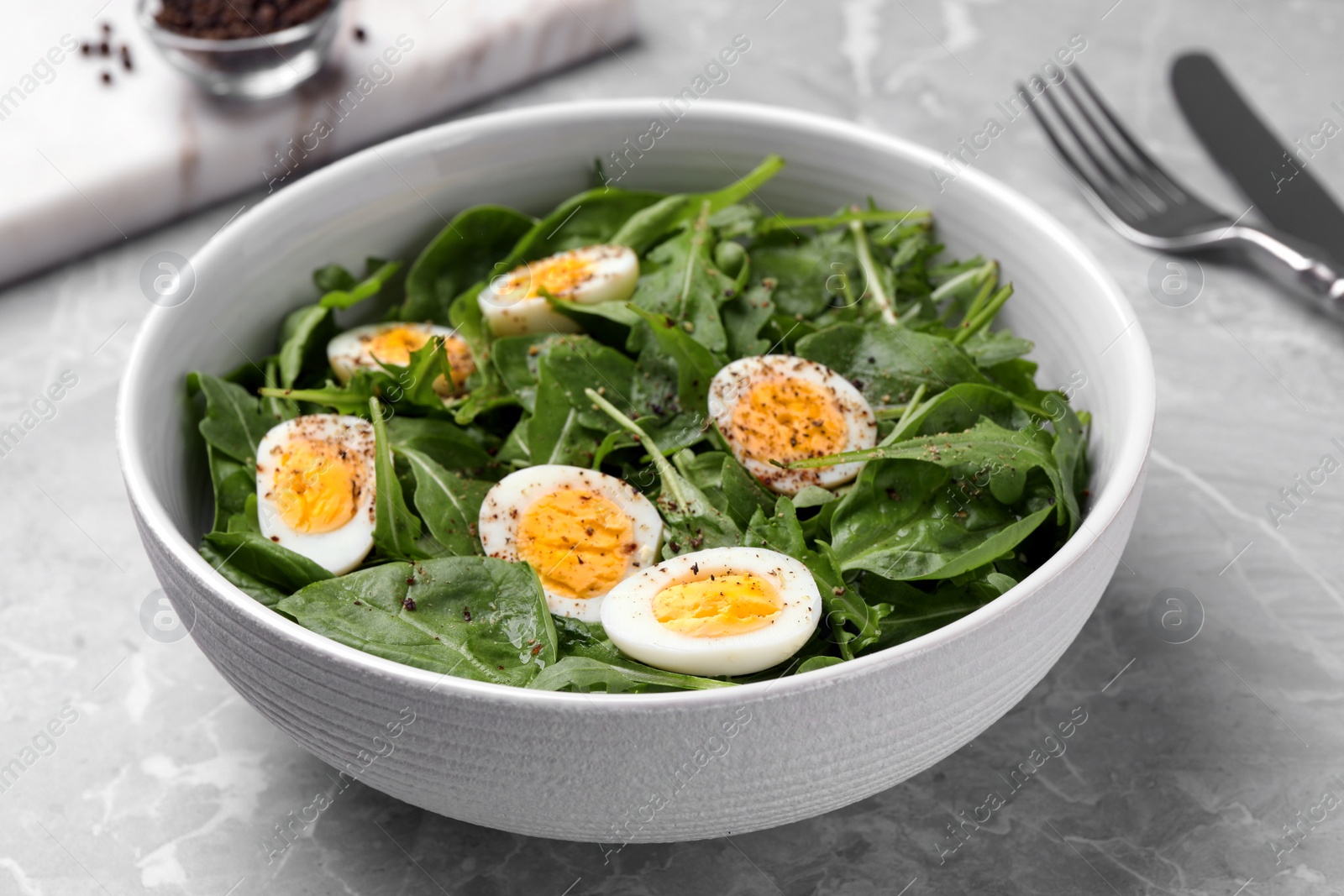 Photo of Delicious salad with boiled eggs and herbs in bowl on light grey marble table, closeup