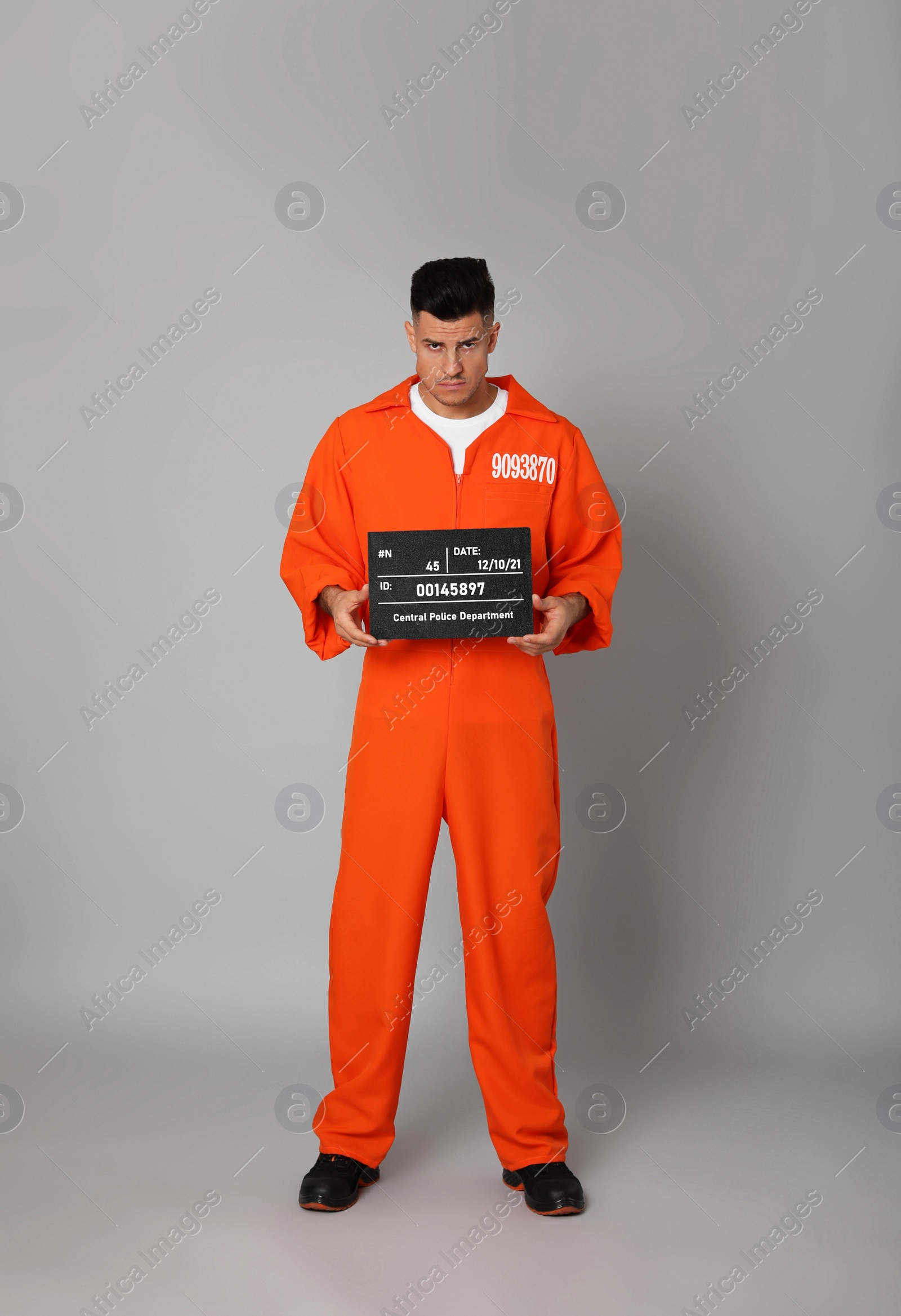 Photo of Prisoner in orange jumpsuit with mugshot letter board on grey background