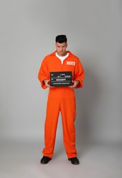 Prisoner in orange jumpsuit with mugshot letter board on grey background