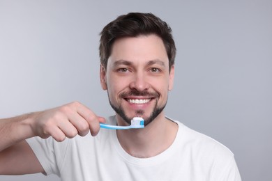 Happy man holding toothbrush on light grey background