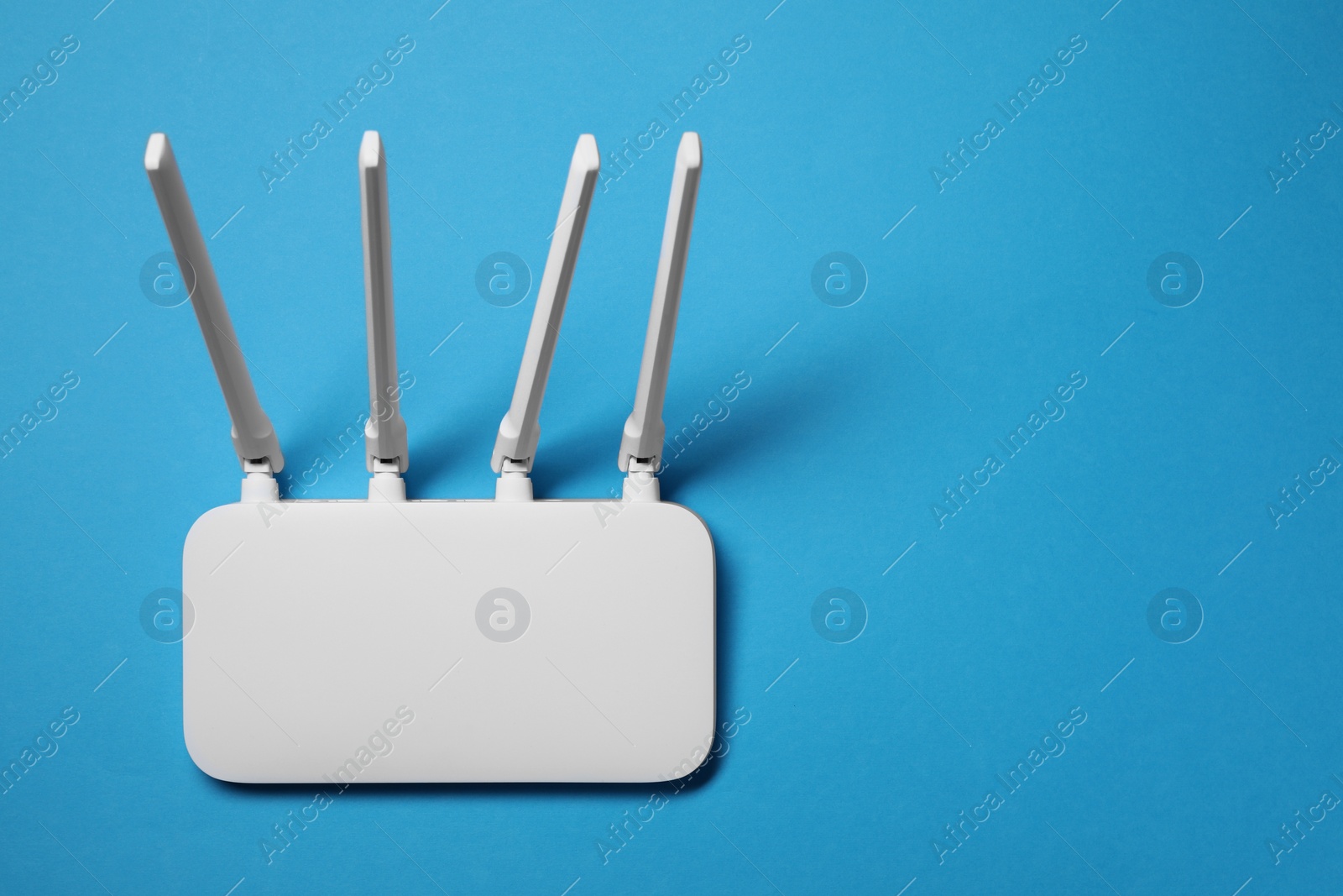 Photo of New white Wi-Fi router on light blue background, top view. Space for text
