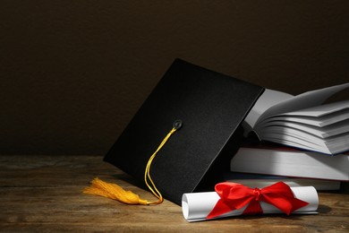Graduation hat, books and diploma on wooden table against brown background, space for text